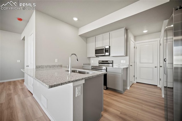 kitchen featuring white cabinets, sink, light stone counters, kitchen peninsula, and stainless steel appliances