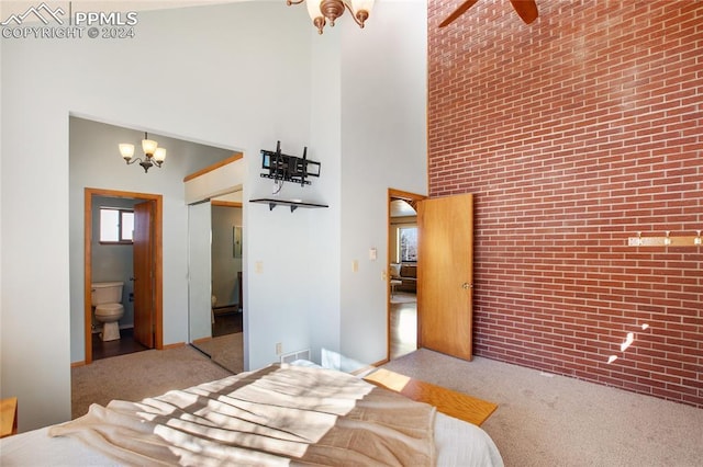 bedroom featuring a high ceiling, ensuite bathroom, carpet floors, brick wall, and a chandelier