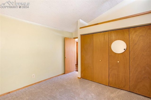 unfurnished bedroom featuring a textured ceiling, light colored carpet, vaulted ceiling, and a closet