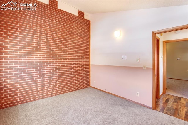 carpeted spare room featuring brick wall