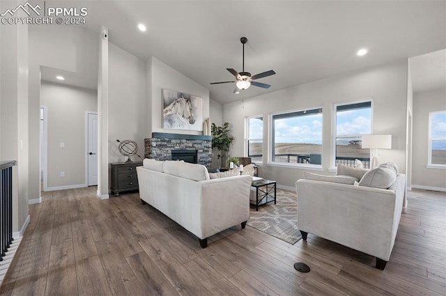 living room with dark wood-type flooring, a stone fireplace, ceiling fan, and lofted ceiling