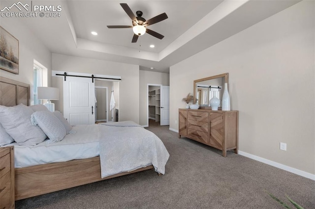 bedroom with carpet, a walk in closet, a tray ceiling, ceiling fan, and a barn door