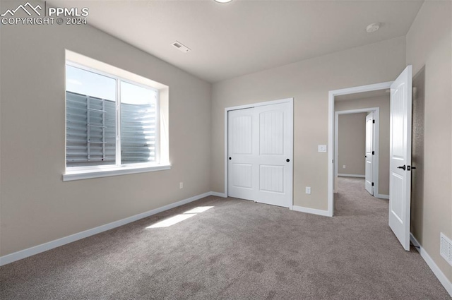 unfurnished bedroom with light colored carpet and a closet