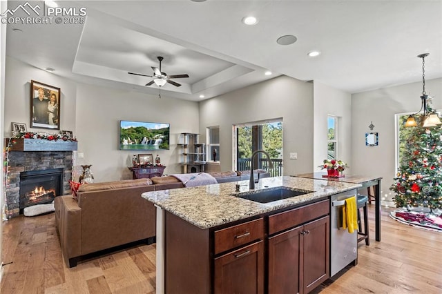 kitchen featuring a center island with sink, sink, stainless steel dishwasher, light stone countertops, and a tray ceiling