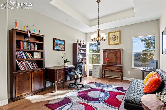 office featuring a notable chandelier, light wood-type flooring, a wealth of natural light, and a tray ceiling