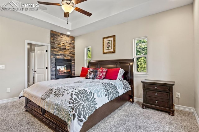 carpeted bedroom with a fireplace, a tray ceiling, and ceiling fan