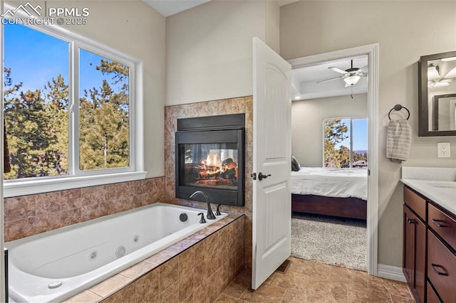 bathroom featuring a multi sided fireplace, vanity, tiled bath, and ceiling fan