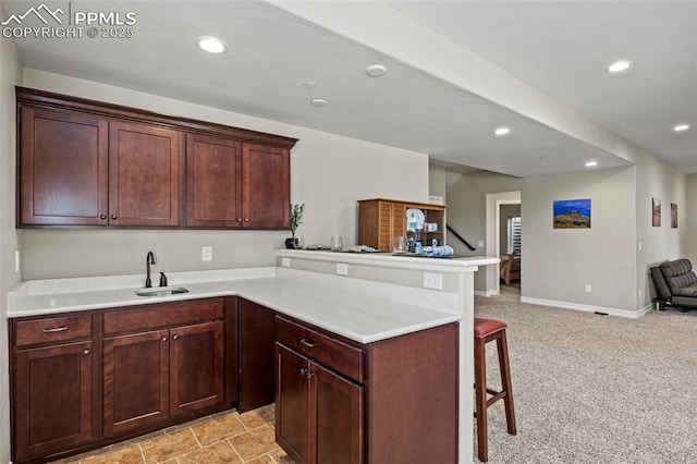 kitchen with a kitchen bar, kitchen peninsula, light carpet, and sink