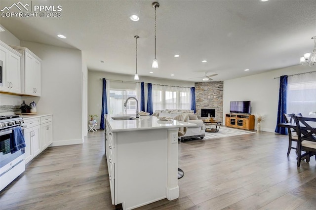 kitchen featuring stainless steel gas range oven, sink, pendant lighting, a center island with sink, and white cabinets