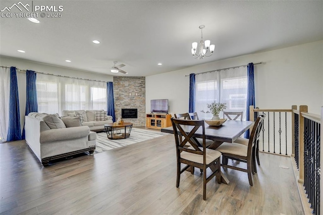 dining room featuring a fireplace, hardwood / wood-style floors, ceiling fan with notable chandelier, and plenty of natural light