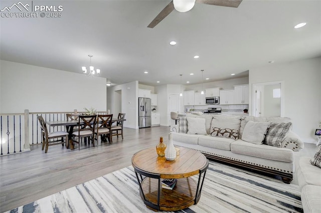 living room with light wood-type flooring and ceiling fan with notable chandelier