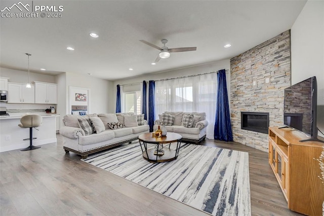 living room with ceiling fan, a stone fireplace, and light wood-type flooring