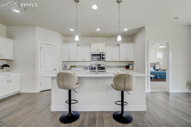 kitchen with a kitchen island with sink, hanging light fixtures, and appliances with stainless steel finishes