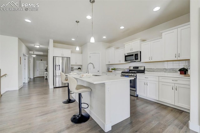 kitchen with pendant lighting, light hardwood / wood-style flooring, an island with sink, white cabinetry, and stainless steel appliances