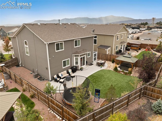 rear view of property with a lawn, a mountain view, a trampoline, central air condition unit, and a gazebo