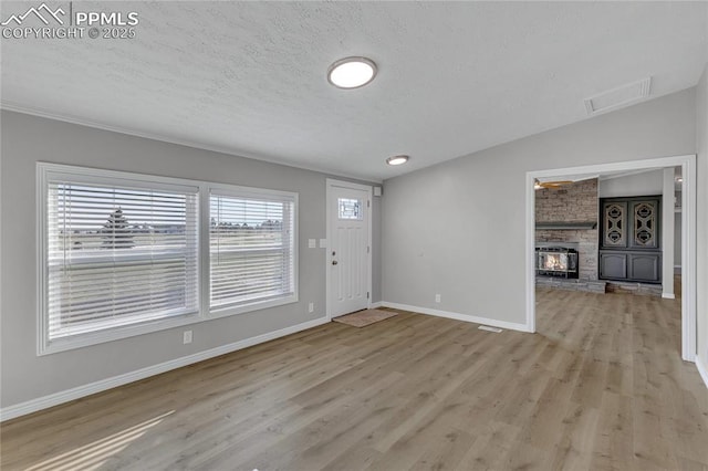 foyer featuring light hardwood / wood-style floors, a wood stove, a textured ceiling, and vaulted ceiling