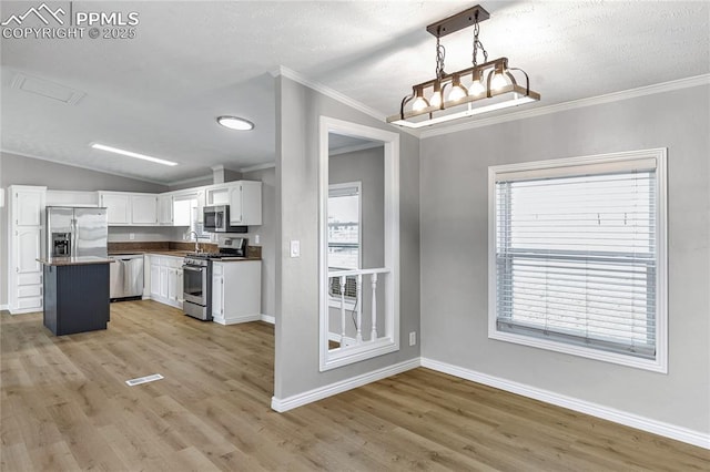 kitchen featuring white cabinetry, vaulted ceiling, decorative light fixtures, appliances with stainless steel finishes, and light wood-type flooring