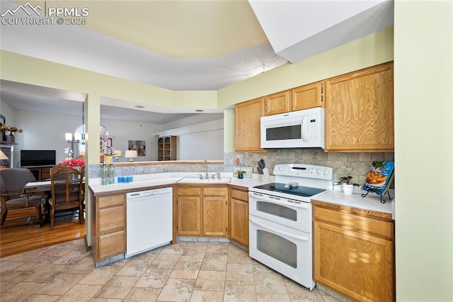 kitchen with sink, white appliances, kitchen peninsula, backsplash, and a notable chandelier