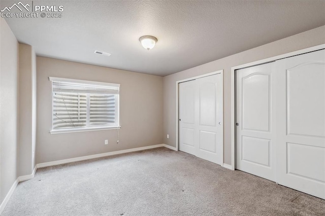 unfurnished bedroom featuring multiple closets, light carpet, and a textured ceiling