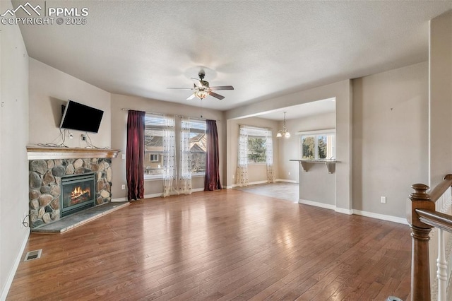 unfurnished living room featuring hardwood / wood-style flooring, ceiling fan with notable chandelier, and a stone fireplace