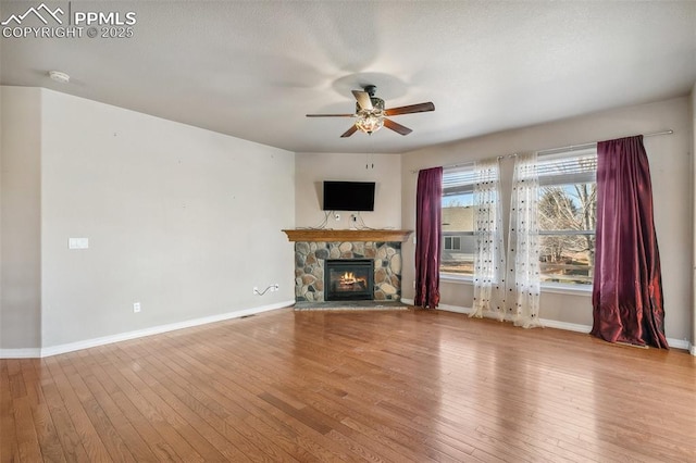 unfurnished living room featuring light wood-type flooring, a stone fireplace, and ceiling fan