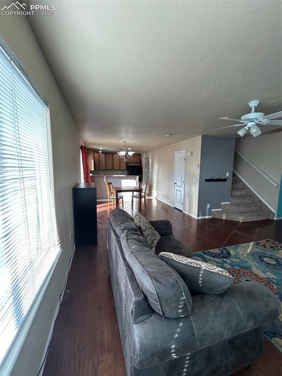 living room featuring a textured ceiling, plenty of natural light, dark wood-type flooring, and ceiling fan with notable chandelier