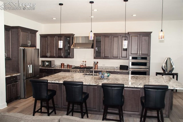 kitchen with appliances with stainless steel finishes, decorative light fixtures, wall chimney exhaust hood, and a large island