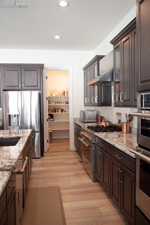 kitchen featuring dark brown cabinetry, sink, stainless steel appliances, light stone counters, and light hardwood / wood-style flooring