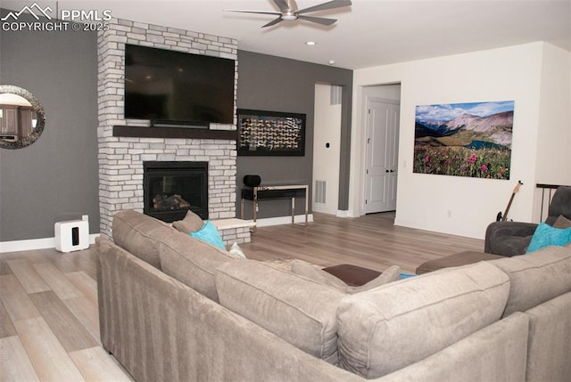 living room with hardwood / wood-style flooring, ceiling fan, and a brick fireplace