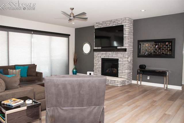 living room featuring ceiling fan, a fireplace, and light hardwood / wood-style flooring