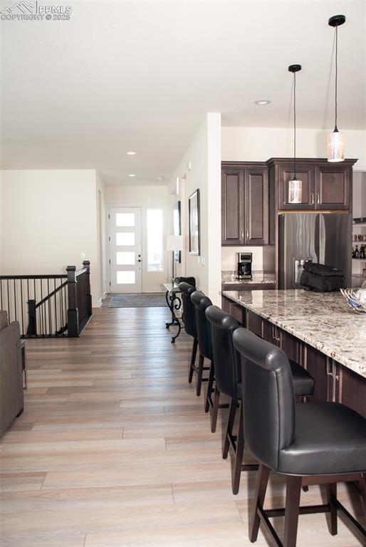 kitchen with light hardwood / wood-style flooring, light stone countertops, decorative light fixtures, dark brown cabinetry, and stainless steel refrigerator