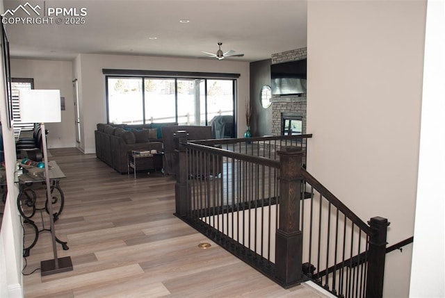 stairway with hardwood / wood-style floors, ceiling fan, and a fireplace