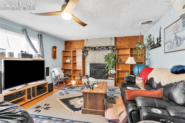 living room featuring a wood stove, wooden walls, ceiling fan, and a textured ceiling