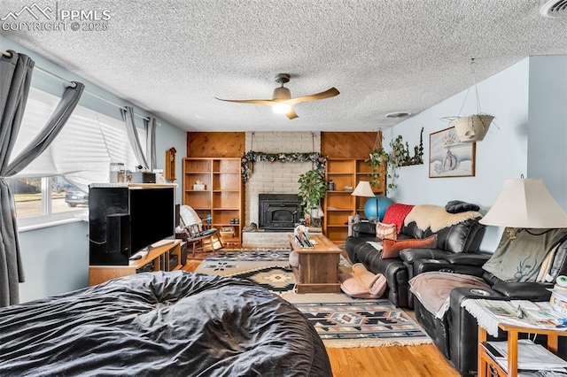 living room with a textured ceiling, hardwood / wood-style flooring, a wood stove, and ceiling fan