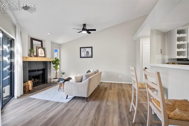 living room featuring ceiling fan, a fireplace, light hardwood / wood-style floors, and lofted ceiling