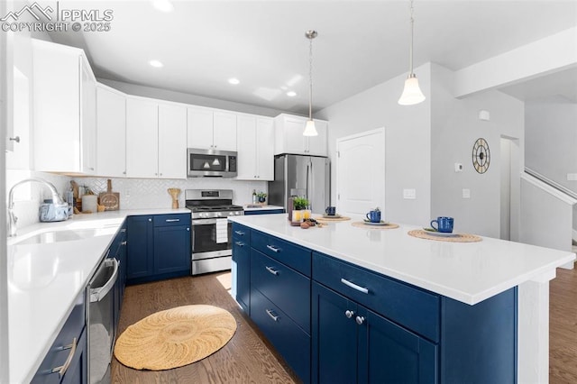 kitchen featuring appliances with stainless steel finishes, sink, blue cabinetry, decorative light fixtures, and a center island