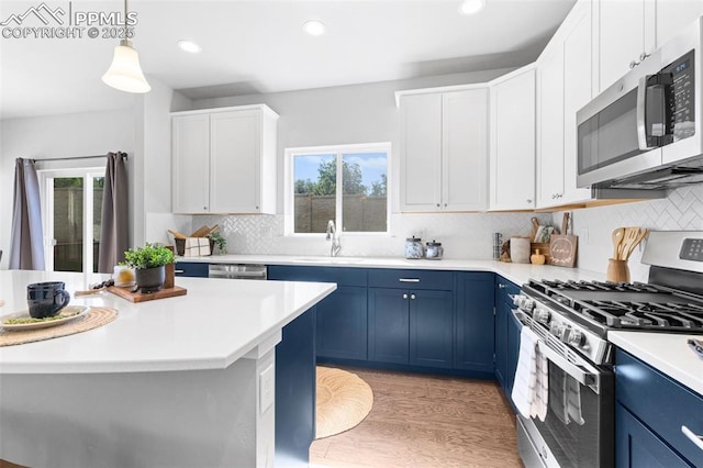 kitchen with blue cabinets, appliances with stainless steel finishes, decorative light fixtures, white cabinets, and light wood-type flooring