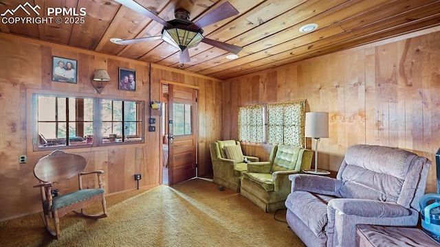 sitting room with wood walls, carpet, wooden ceiling, and ceiling fan