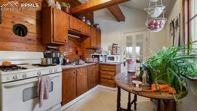 kitchen with wood walls, sink, beamed ceiling, and white appliances