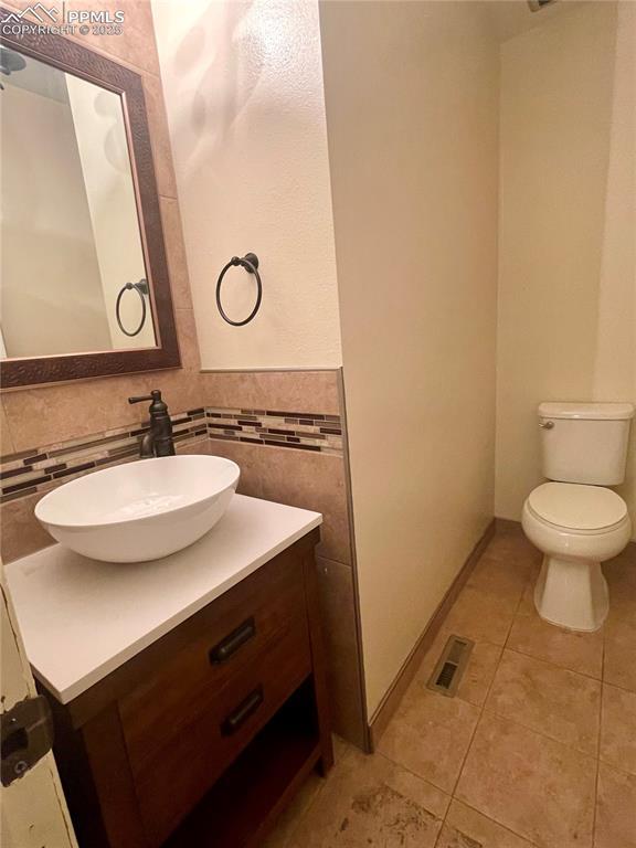 bathroom with tile patterned flooring, vanity, toilet, and tile walls