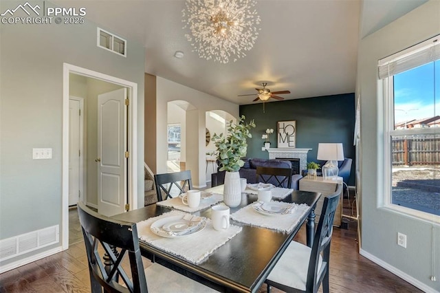 dining area with ceiling fan with notable chandelier and dark hardwood / wood-style floors