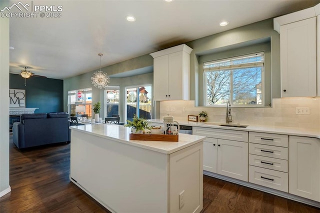 kitchen with white cabinetry, dark hardwood / wood-style floors, pendant lighting, ceiling fan with notable chandelier, and sink