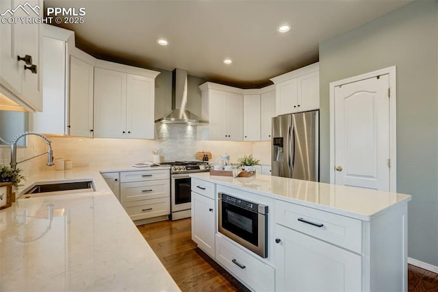 kitchen featuring sink, appliances with stainless steel finishes, wall chimney range hood, and white cabinetry