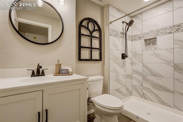 bathroom with vanity, toilet, and tiled shower