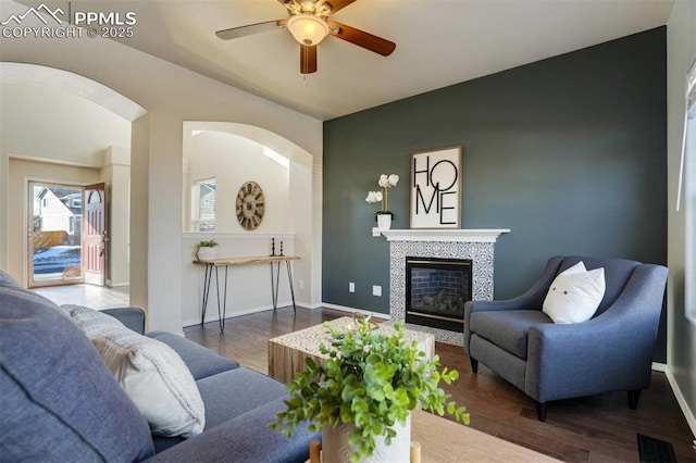 living room with dark wood-type flooring, a tile fireplace, and ceiling fan