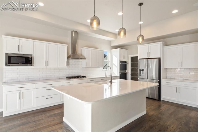 kitchen with a center island with sink, white cabinetry, wall chimney range hood, and appliances with stainless steel finishes