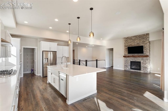 kitchen with a kitchen island with sink, white cabinets, a fireplace, appliances with stainless steel finishes, and decorative light fixtures