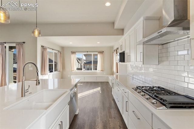 kitchen featuring pendant lighting, wall chimney range hood, sink, white cabinetry, and stainless steel appliances