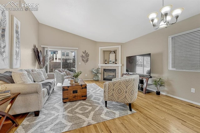 living room featuring a tile fireplace, wood-type flooring, vaulted ceiling, and an inviting chandelier