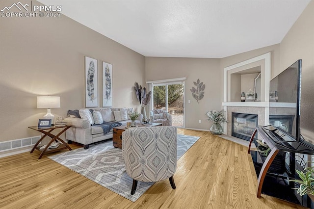 living room featuring light wood-type flooring, a tile fireplace, and vaulted ceiling